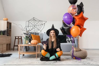 Cadılar Bayramı 'nda evde oturan tarot kartları ve balonlarla cadı gibi giyinmiş genç bir kadın.