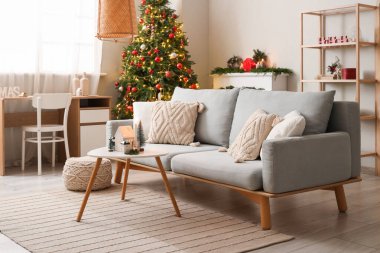 Gri kanepesi, kahve masası ve Noel ağacı olan şenlikli oturma odasının içinde.