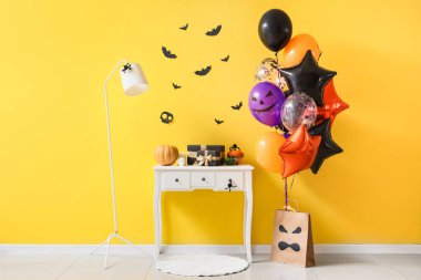 Colorful Halloween balloons with pumpkins and gift boxes on table near yellow wall clipart