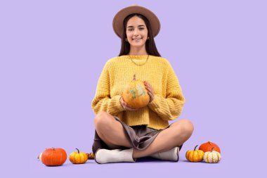 Mor arka planda oturan bir sürü balkabağı olan güzel, genç bir kadın.