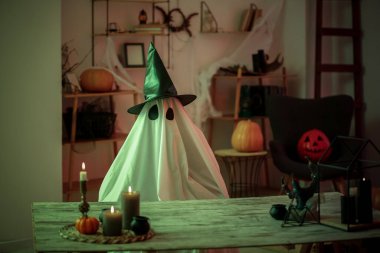 Cadılar Bayramı kostümü giymiş cadı şapkalı ve evde mum yakan biri.