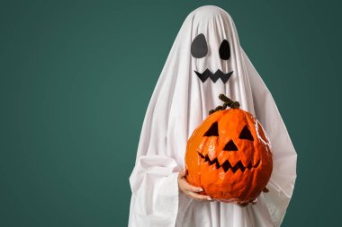 Cadılar Bayramı kostümlü yeşil arka planda oyulmuş balkabağı olan kişi.