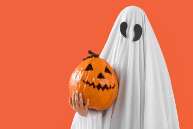 Cadılar Bayramı kostümlü turuncu arka planda oyulmuş balkabağı olan kişi.