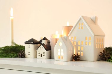 Noel için dekore edilmiş odanın ışık duvarının yanındaki rafta ev şeklinde tutucuları olan yanan mumlar, yakın plan.