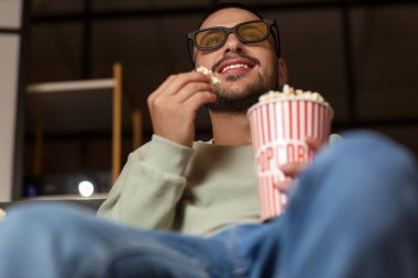 Üç boyutlu gözlüklü ve patlamış mısırlı genç adam akşamları evdeki kanepede film izliyor.