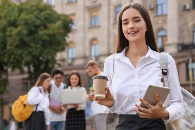 Üniversitenin yakınında kahve fincanı ve tablet bilgisayarı olan bir kız öğrenci.