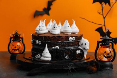 Tatlı cadılar bayramı pastası, hayaletler, gözler ve kelime BOO siyah masada turuncu arka planda