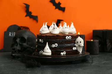 Tatlı cadılar bayramı pastası, hayaletler, gözler ve kafatası siyah masada turuncu arka planda.