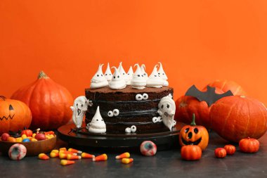 Tatlı cadılar bayramı pastası, hayaletler, gözler ve mısır şekeri siyah masada turuncu arka planda.