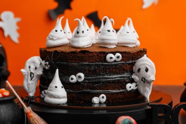 Tatlı pasta, hayaletler, gözler ve cadılar bayramı süslemeleri siyah masada turuncu arka planda.