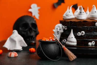 Tatlı pasta, hayaletler, gözler ve cadılar bayramı süslemeleri siyah masada turuncu arka planda.