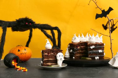 İçinde hayaletler, mısır şekerlemeleri ve sarı arka planda siyah masanın üzerinde korkunç örümceklerin olduğu lezzetli bir Cadılar Bayramı pastası.