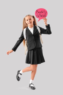 Okul üniformalı şirin bir kız elinde konuşma balonu tutarak gri arka planda okula geri dönüyor.