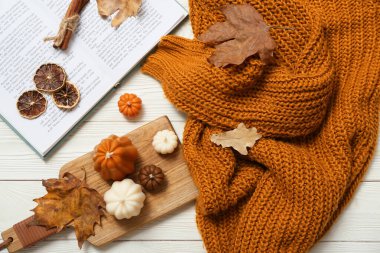 Balkabağı şeklinde mumlar, kitap ve ahşap arka planda sıcak süveter içeren kompozisyon