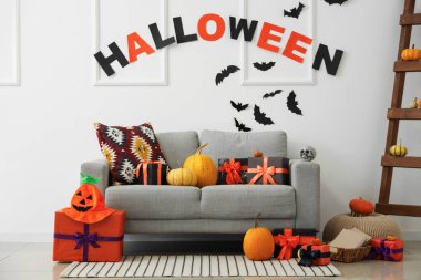 İçinde gri kanepe, Cadılar Bayramı süslemeleri ve hediye kutuları olan şenlikli bir oturma odası.