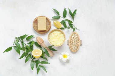 Bowl of lemon body scrub with massage brush, juicer and soap on white background