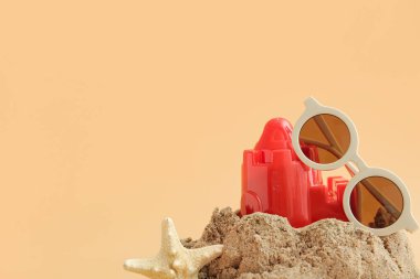 Plaj oyuncağı, deniz yıldızı ve turuncu arka planda güneş gözlüğü olan kumdan kale