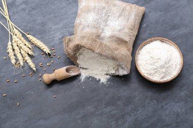 Siyah grunge arka planında buğday unuyla çuval ve kase.