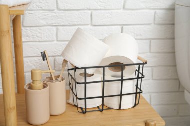 Tuvalet kağıdı ruloları ve banyo malzemelerinin bulunduğu sepet tuğla duvarın yanındaki ahşap raflarda, yakın plan.