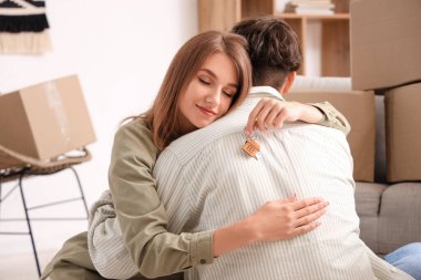 Anahtarları olan genç bir çift yeni evlerinde birbirlerine sarılıyorlar.