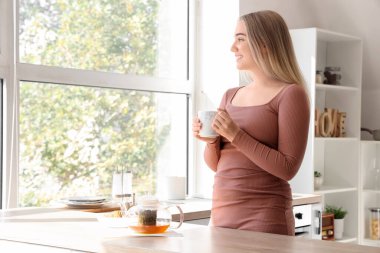 Mutfakta bir fincan sıcak çayla genç bir kadın.