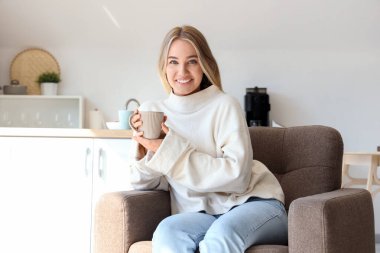 Bir fincan sıcak çayla mutfakta oturan genç bayan.