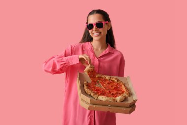 Güneş gözlüklü, pembe arka planda lezzetli pizzalı güzel bir kadın.