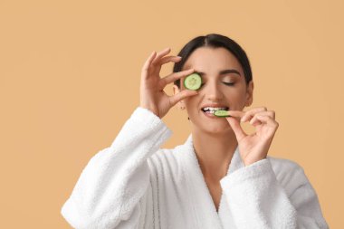 Bej arka planda salatalık yiyen genç bir kadın.