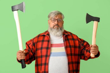 Yeşil arka planda baltaları olan olgun oduncu portresi