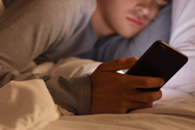Cep telefonlu genç adam geceleri yatakta uyuyor, yakın plan.