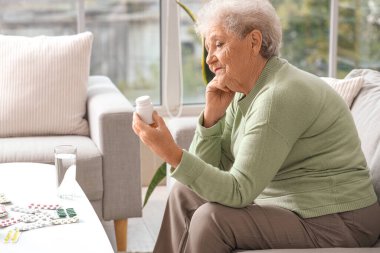 Evde ilaç şişesi olan düşünceli bir yaşlı kadın.