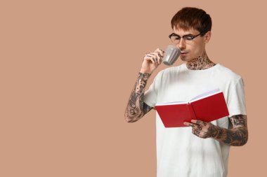 Kahverengi arka planda kitap ve bir fincan kahve olan dövmeli genç bir adam.