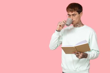 Pembe arka planda kitap ve bir fincan kahve olan dövmeli genç bir adam.