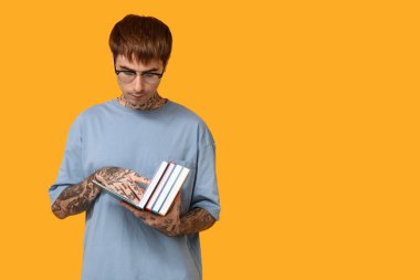 Sarı arka planda kitap okuyan dövmeli genç bir adam.