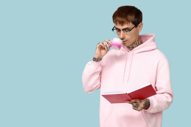 Mavi arka planda kitap ve bir fincan kahve olan dövmeli genç bir adam.