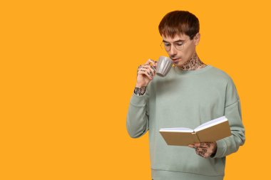 Sarı arka planda kitap ve bir fincan kahve olan dövmeli genç bir adam.