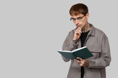 Gri arkaplan üzerine kitap okuyan dövmeli genç adam.
