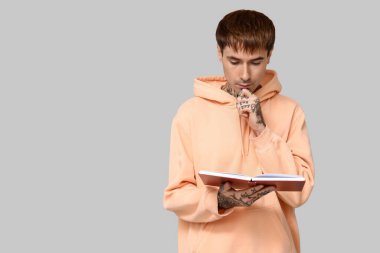 Gri arkaplan üzerine kitap okuyan dövmeli genç adam.