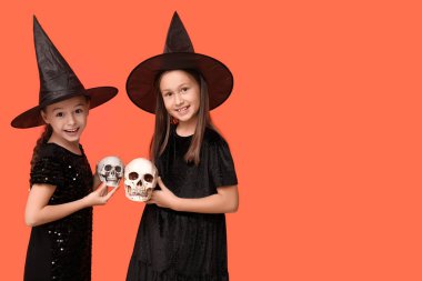 Cadılar Bayramı için giyinmiş şirin kızlar. Turuncu arka planda insan kafatasları olan cadılar.