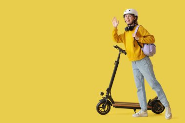 Sarı arka planda modern elektrikli scooter 'ı olan kasklı güzel bir genç kadın.
