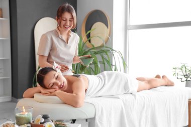 Masaj terapisti spa salonunda genç bir kadının sırtına çamur sürüyor.