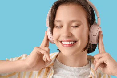 Kulaklıklı genç kadın mavi arka planda müzik dinliyor, yakın plan.