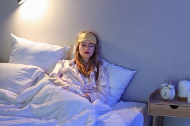 Geceleri yatak odasında uykusuzluk çeken uyku maskeli genç bir kadın.
