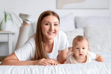 Güzel, genç, mutlu bir anne ve küçük sevimli bir bebek yatak odasında yatıyor.