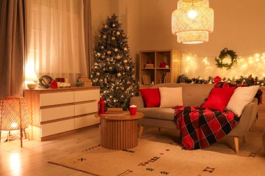 Geceleri tatil için süslenmiş kanepesi ve Noel ağacı olan rahat bir oturma odası.