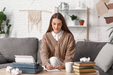 Evdeki kanepede daktilo ve kitaplarla yazan güzel, mutlu bir kadın yazar.