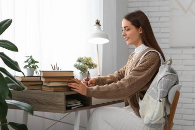 Sırt çantaları ve kitaplarla dolu bir odada ders çalışan güzel, mutlu bir kız öğrenci.