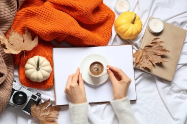 Bir fincan lezzetli balkabağı kahveli, kitaplı ve sıcak kazaklı kadın elleri.