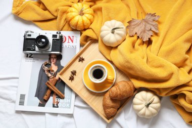 Bir fincan lezzetli balkabağı kahvesi, sonbahar süslemeleri, kruvasanlar ve sıcak ekoseli ev manzaralı.