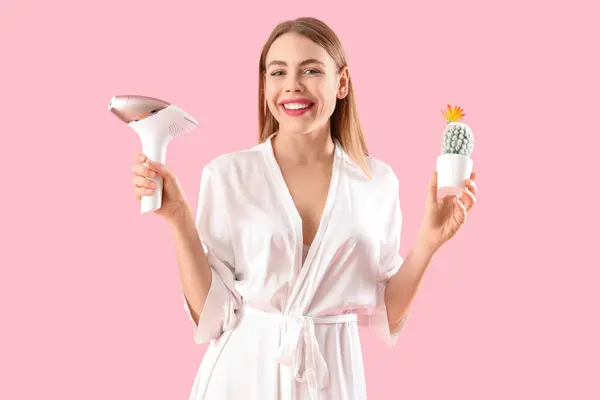 stock image Beautiful young woman with modern photoepilator and cactus on pink background